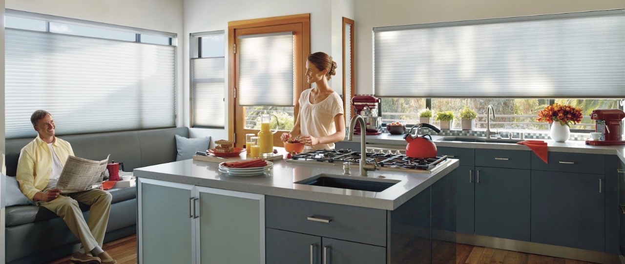 Husband reading the paper and wife in kitchen both smiling in kitchen. Duette shades in the windows